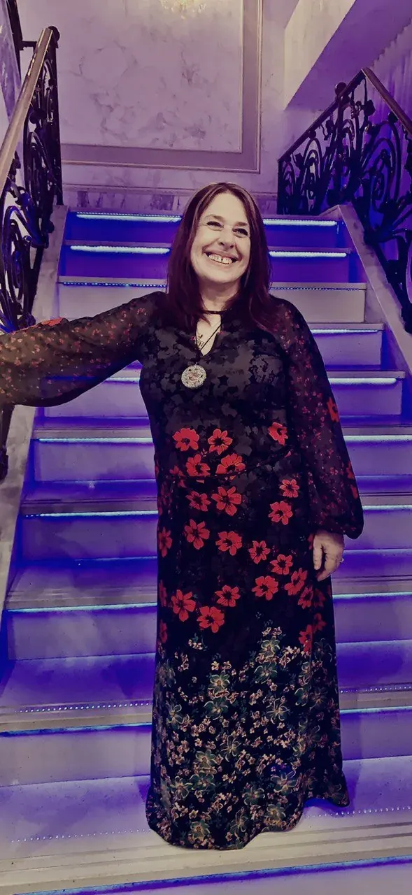 Smiling woman in a flower-patterned dress on indoor stairs for reflective adult storytelling Smiling woman in a flower-patterned dress on indoor stairs for reflective adult storytelling