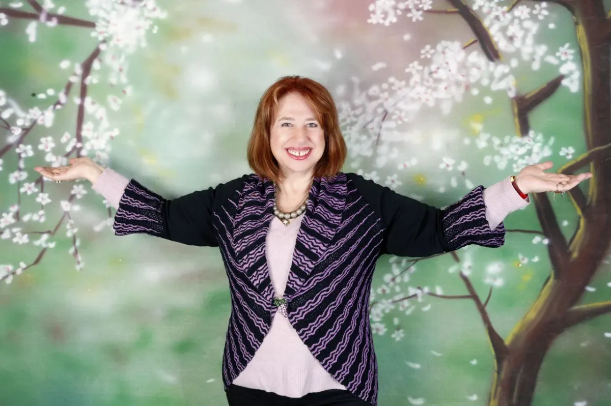 Smiling red-haired woman with arms outstretched against a floral backdrop, for a self-discovery hub page.