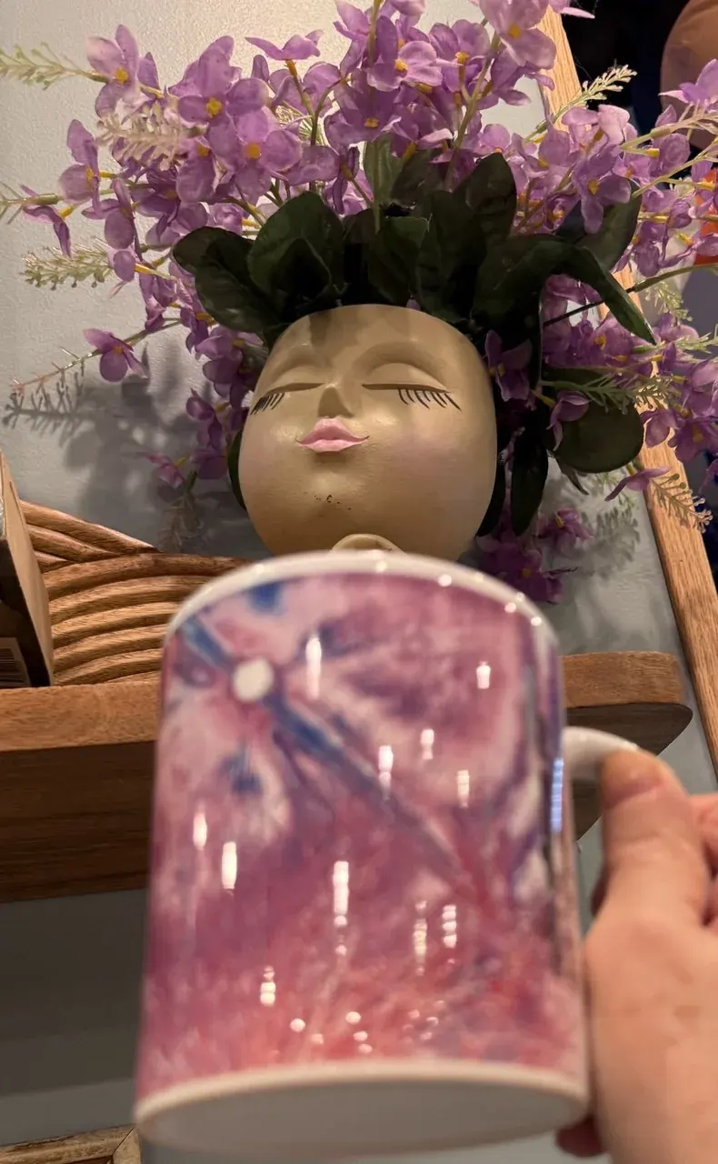 Decorative face planter with closed eyes, purple flowers, and a hand holding a blurred mug for a mythic storytelling page Decorative face planter with closed eyes, purple flowers, and a hand holding a blurred mug for a mythic storytelling page